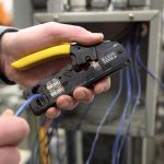 A close up on the hands of a person holding the KLEIN TOOLS Ratcheting Data Cable Crimper / Stripper / Cutter and putting a cable into it