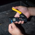 A close up on the hands of a person holding the KLEIN TOOLS Ratcheting Data Cable Crimper / Stripper / Cutter and putting a cable into it