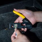 A close up on the hands of a person holding the KLEIN TOOLS Ratcheting Data Cable Crimper / Stripper / Cutter and putting in the wires within a stripped cable ready for crimping
