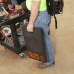 KLEIN TOOLS Tradesman Pro Standard Kneeling Pad being held by the handle by a worker on-site