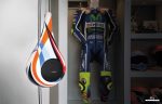 A Garvan Goccia Speaker suspended from a Goccia floor fixing system - Drudi finish. Shown next to a matching MotoGP motorcycle suit.