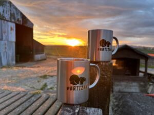 Two Partizan Security mugs shown in front of a sunset in rural setting